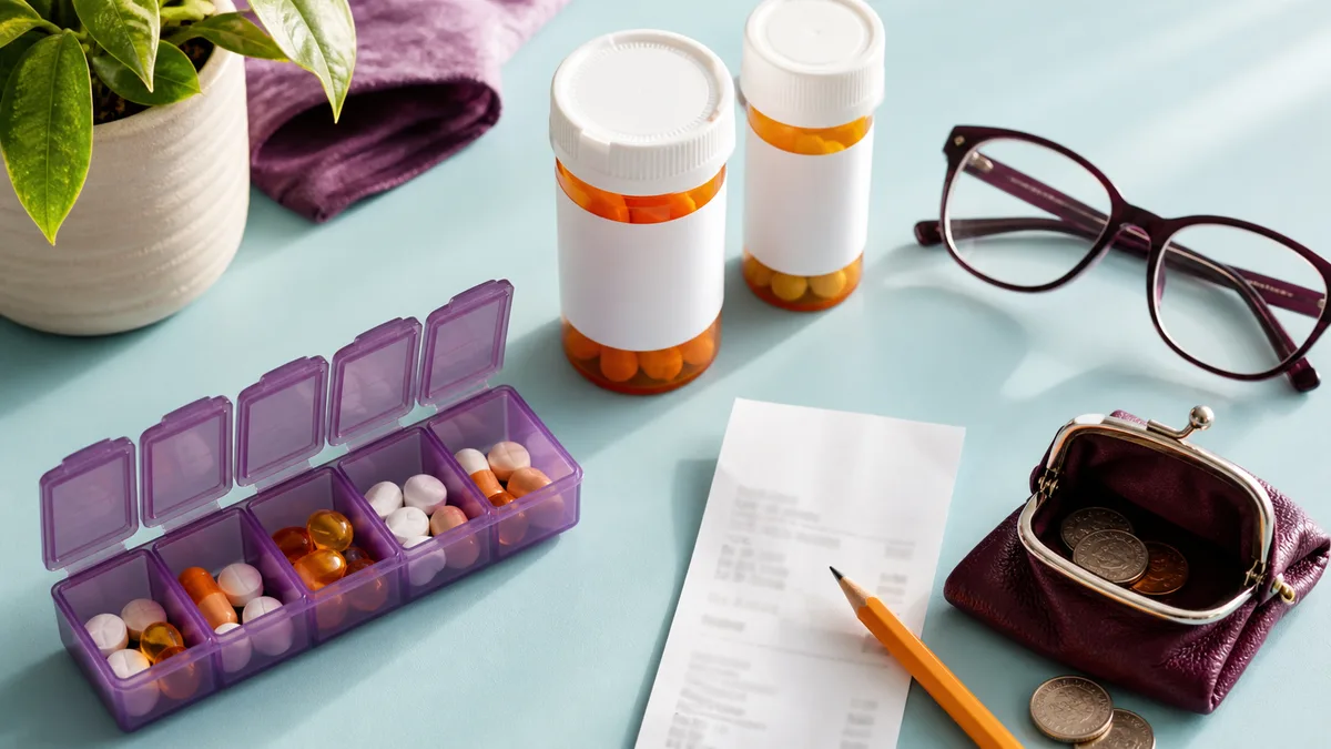 A pill organizer, medicine bottles, reading glasses, and a receipt sit on a bright counter.